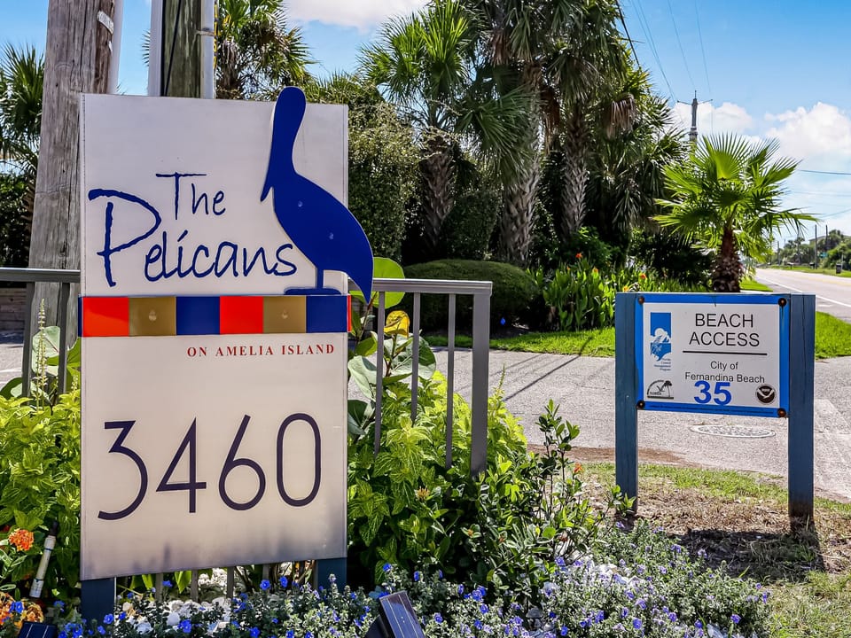 The Pelicans on Amelia Island is located at 3460, with convenient access to Fernandina Beach. The property features lush tropical landscaping with palm trees and a welcoming entrance.