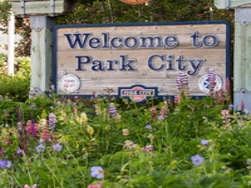 A charming welcome sign greets visitors to Park City, framed by vibrant wildflowers in full bloom, marking the entrance to this historic mountain town.
