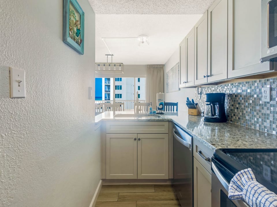 Step into your fully equipped kitchen with coastal charm—granite counters, ocean-inspired backsplash, and a balcony just beyond where you can sip your morning coffee with a view.