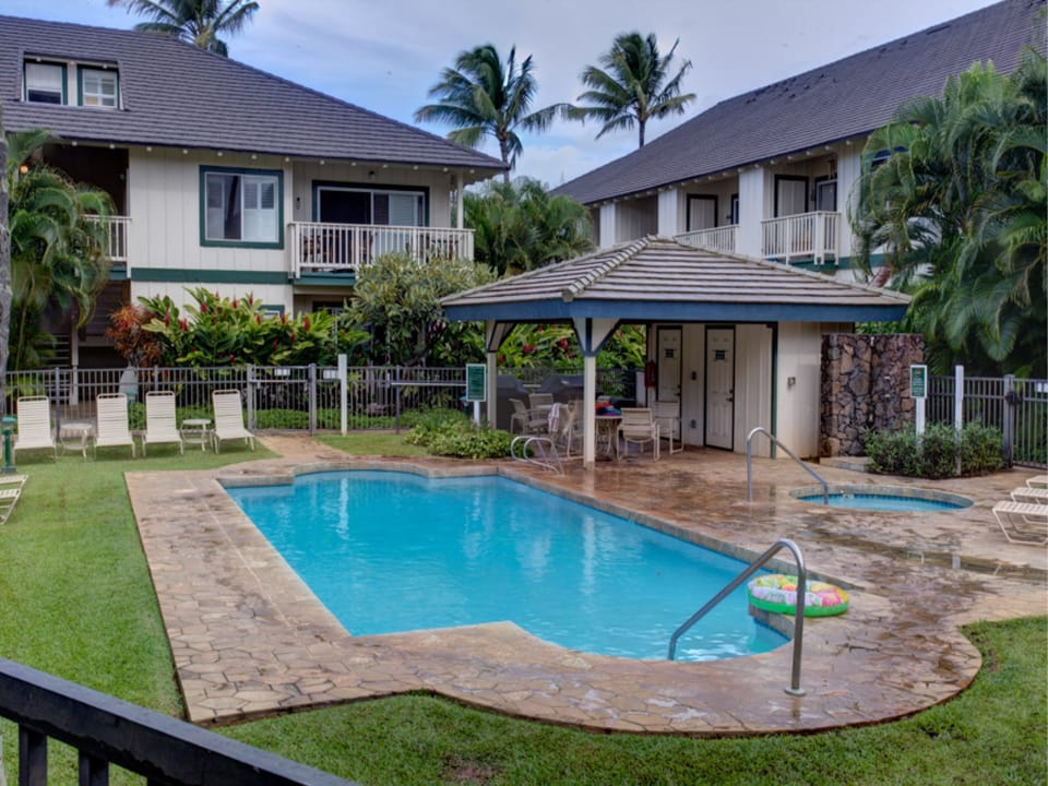 A tranquil pool area set within lush tropical surroundings, featuring a covered pavilion and multiple lounge chairs on manicured lawns, offering a peaceful escape during your Hawaiian getaway.
