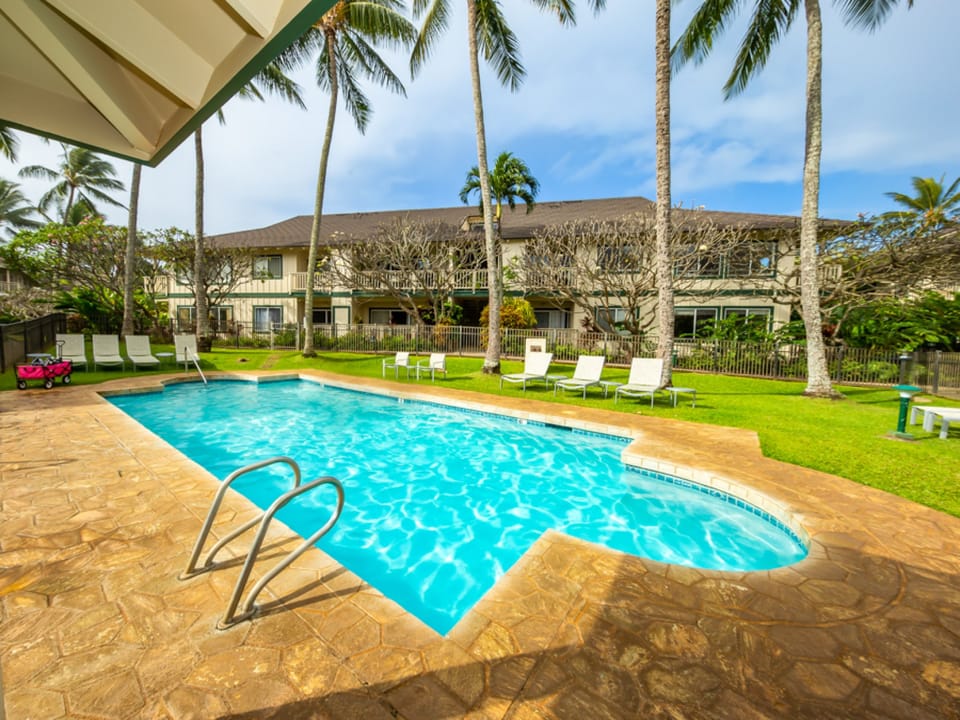 The sparkling pool set among swaying palms and lush grass, with the main building as your peaceful backdrop and loungers ready for your tropical escape.