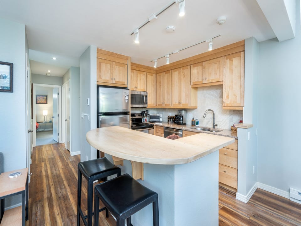 Your open-concept kitchen features warm wood cabinetry, granite countertops, and modern appliances, with a curved breakfast bar perfect for morning coffee or casual meals.