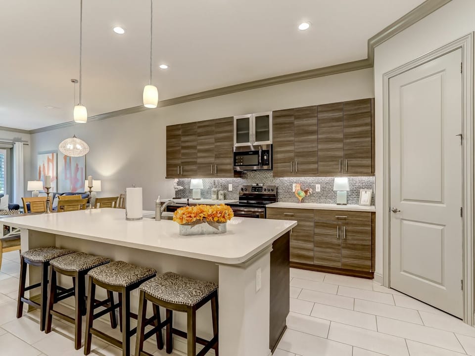 Beautifully designed kitchen featuring sleek wood-grain cabinetry, bright white countertops, and a spacious island. Modern backsplash and warm pendant lighting create the perfect gathering space.