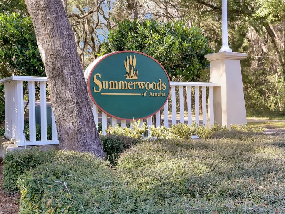 The property's welcoming entrance sign stands amidst beautiful natural landscaping and mature trees, creating an inviting arrival experience at Summerwoods of Amelia.