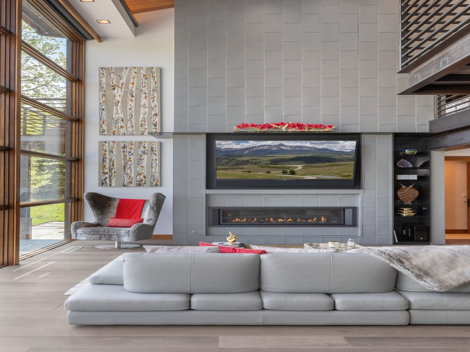 Settle into the plush sofa and enjoy the warmth of your fireplace beneath soaring ceilings and stunning natural light from floor-to-ceiling windows.