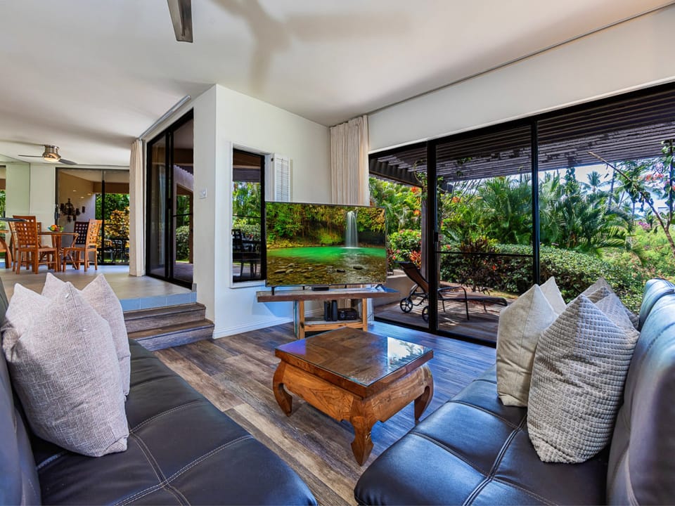 Sink into plush leather seating as your gaze drifts through open glass doors to lush tropical gardens. The open-concept design invites fresh breezes indoors, blending your living space seamlessly with nature.