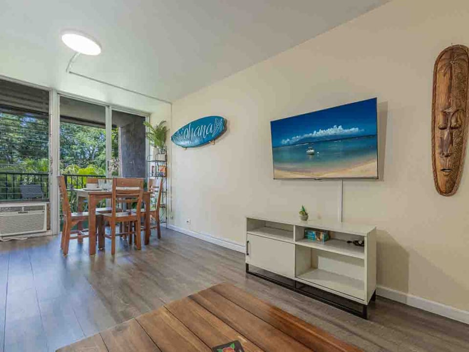 Light-filled living and dining area with tropical décor. Sliding doors open to a private lanai overlooking lush greenery.