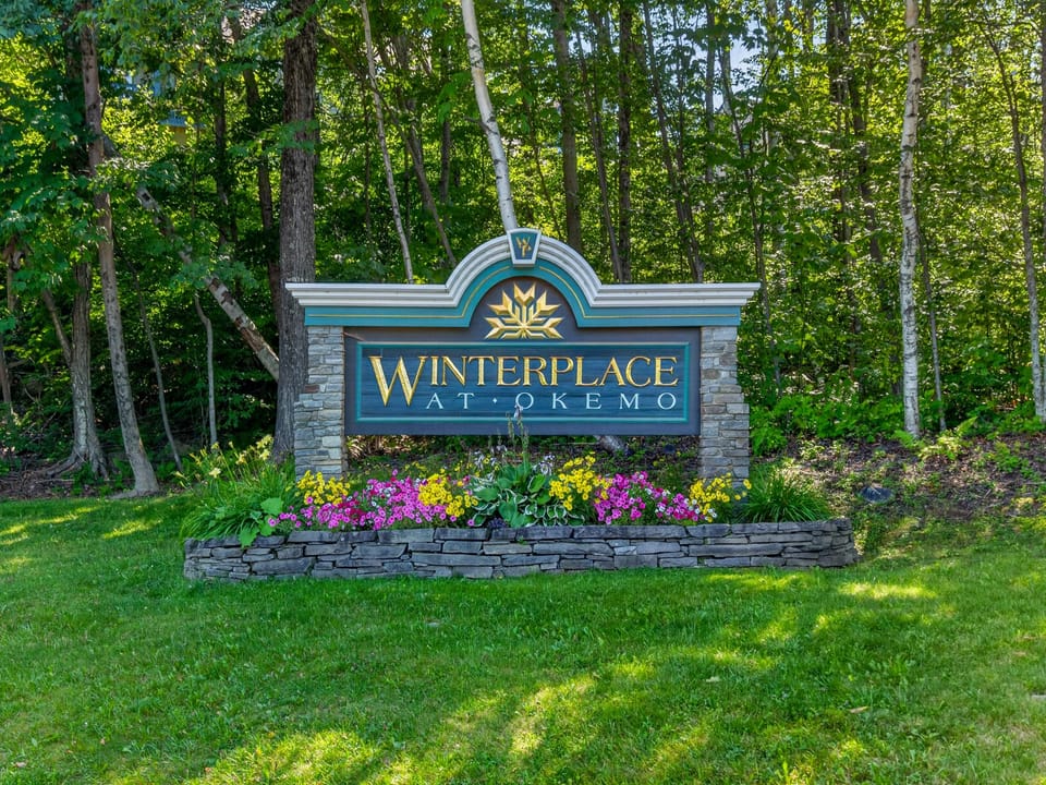 The entrance marker at Winterplace at Okemo welcomes visitors to a wooded mountain setting surrounded by lush summer foliage.