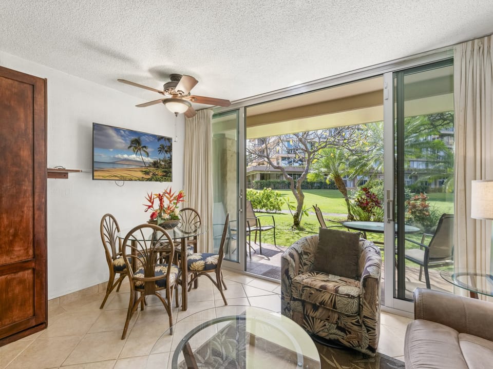Relax in your inviting living area with garden views framed by sliding glass doors, where tropical breezes and lush greenery create a serene escape just steps from your lanai.