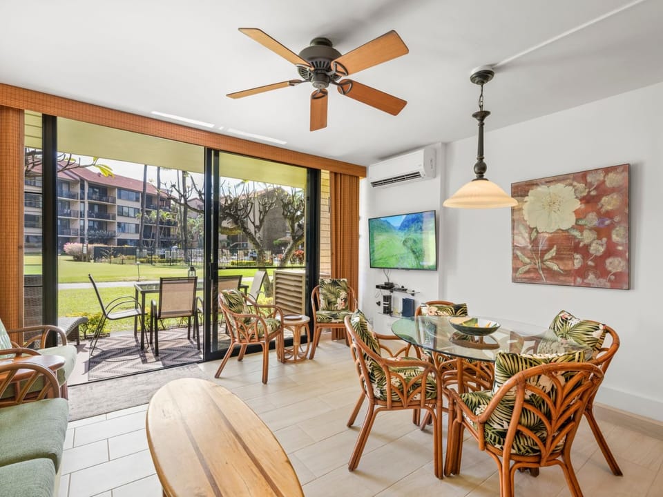 Relax in your tropical-inspired living area with a dining table for six, a ceiling fan, and sliding doors opening to your private patio overlooking lush green grounds.