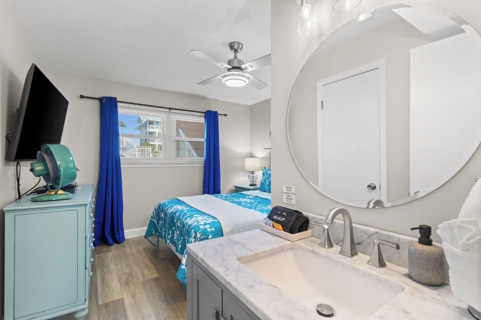 Sunny coastal room with TV, ceiling fan, and an in-room marble vanity.