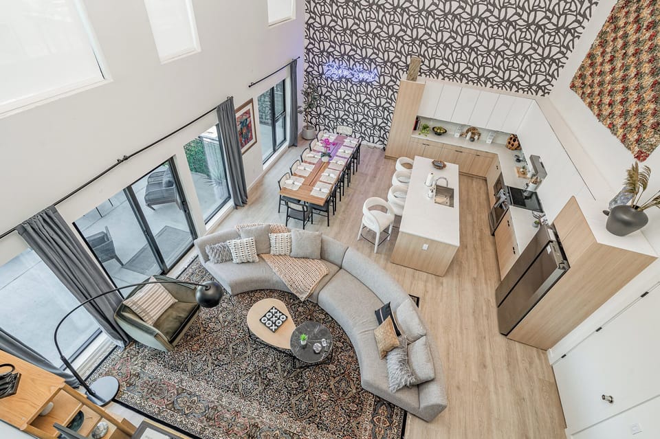 Main Level: Bright open floor living area featuring a large smart flat-screen TV, designer furnishings, and entrance to a large private patio.