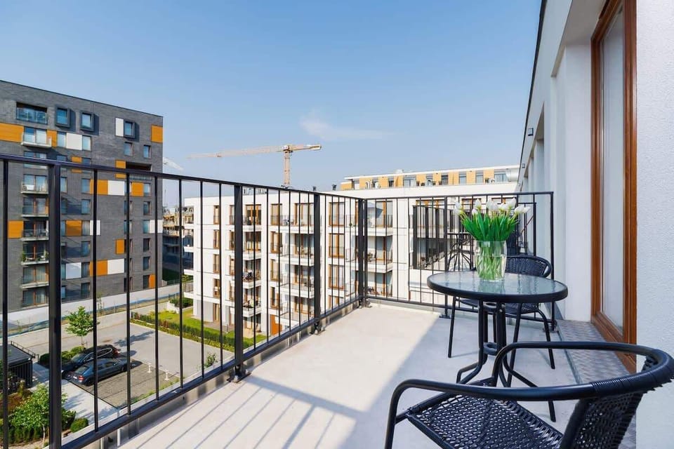 A balcony with a small table and chairs, offering a view of a modern residential area with greenery and other buildings.