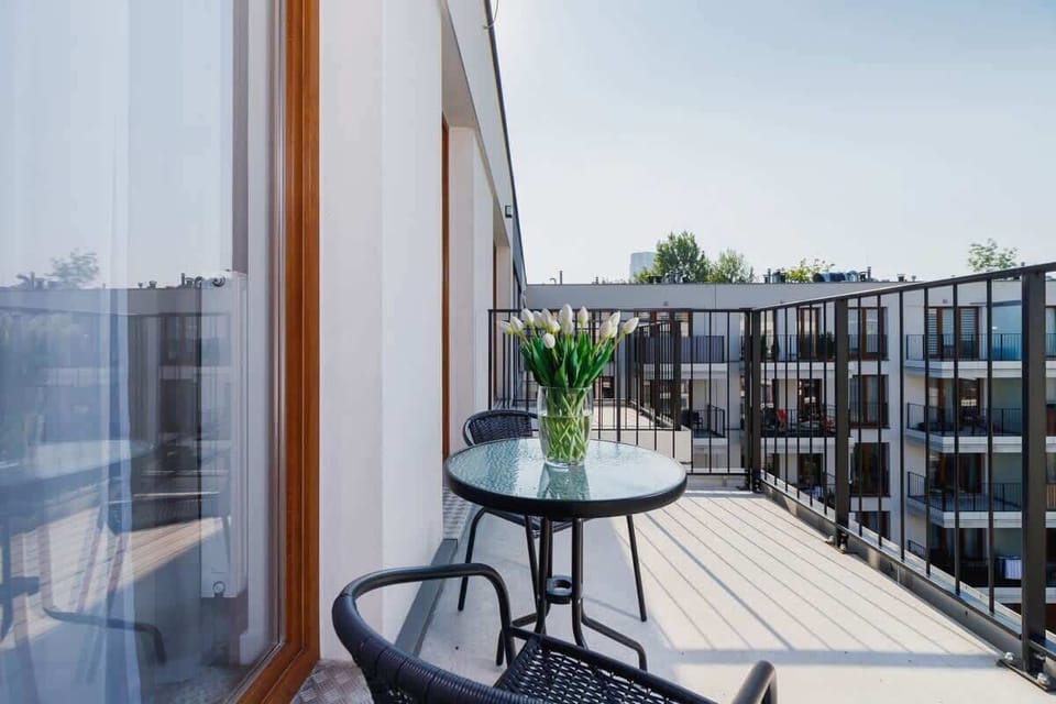 A balcony with a modern, minimalistic design, offering outdoor seating and a view of nearby buildings and greenery.