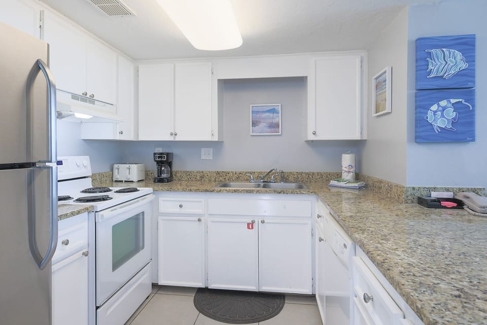 The kitchen features modern appliances, granite countertops, and coastal decor, perfect for dining with a beach view