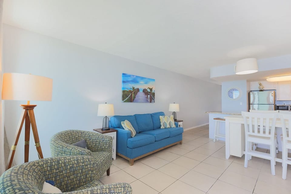 The living area features a blue sofa, stylish chairs, and a view of the kitchen, perfect for relaxation and entertainment