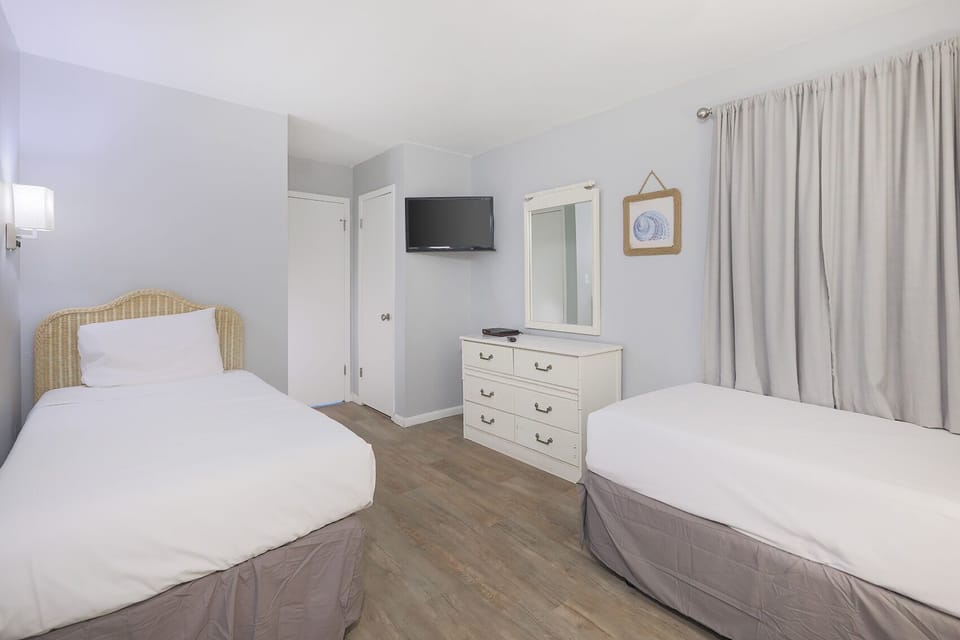 This guest bedroom features two comfortable beds, a wall-mounted TV, and soft gray tones for a relaxing atmosphere