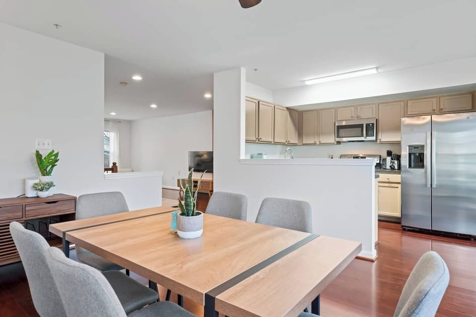 Modern dining space with sleek wooden table, soft gray chairs and cozy kitchen.