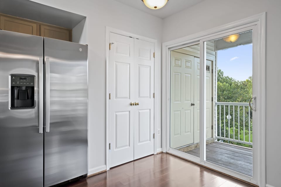 Sleek stainless fridge beside a sunlit balcony entrance, promising fresh air.