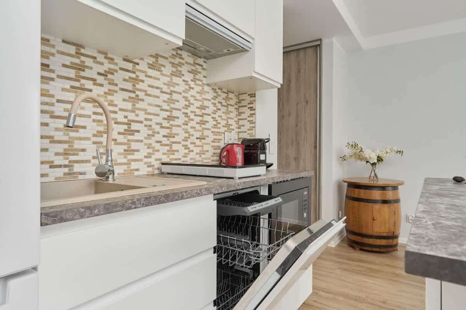 A modern kitchen with white cabinets, a patterned backsplash, and stainless steel appliances.
