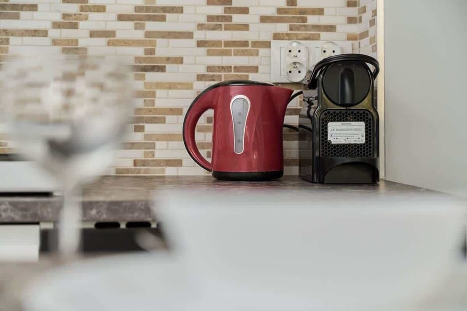 A close-up of a kitchen countertop, featuring a red kettle, a coffee maker, and a decorative backsplash.
