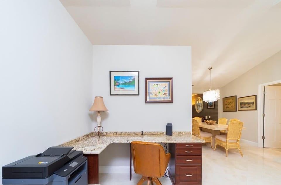 Built-in granite desk with dark wood drawers, swivel leather chair, and two framed prints overhead.