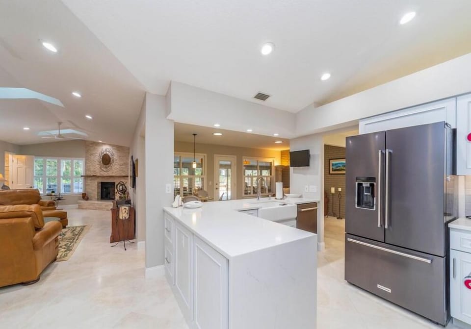 White quartz island with farmhouse sink faces a stainless steel French-door refrigerator and open living room.