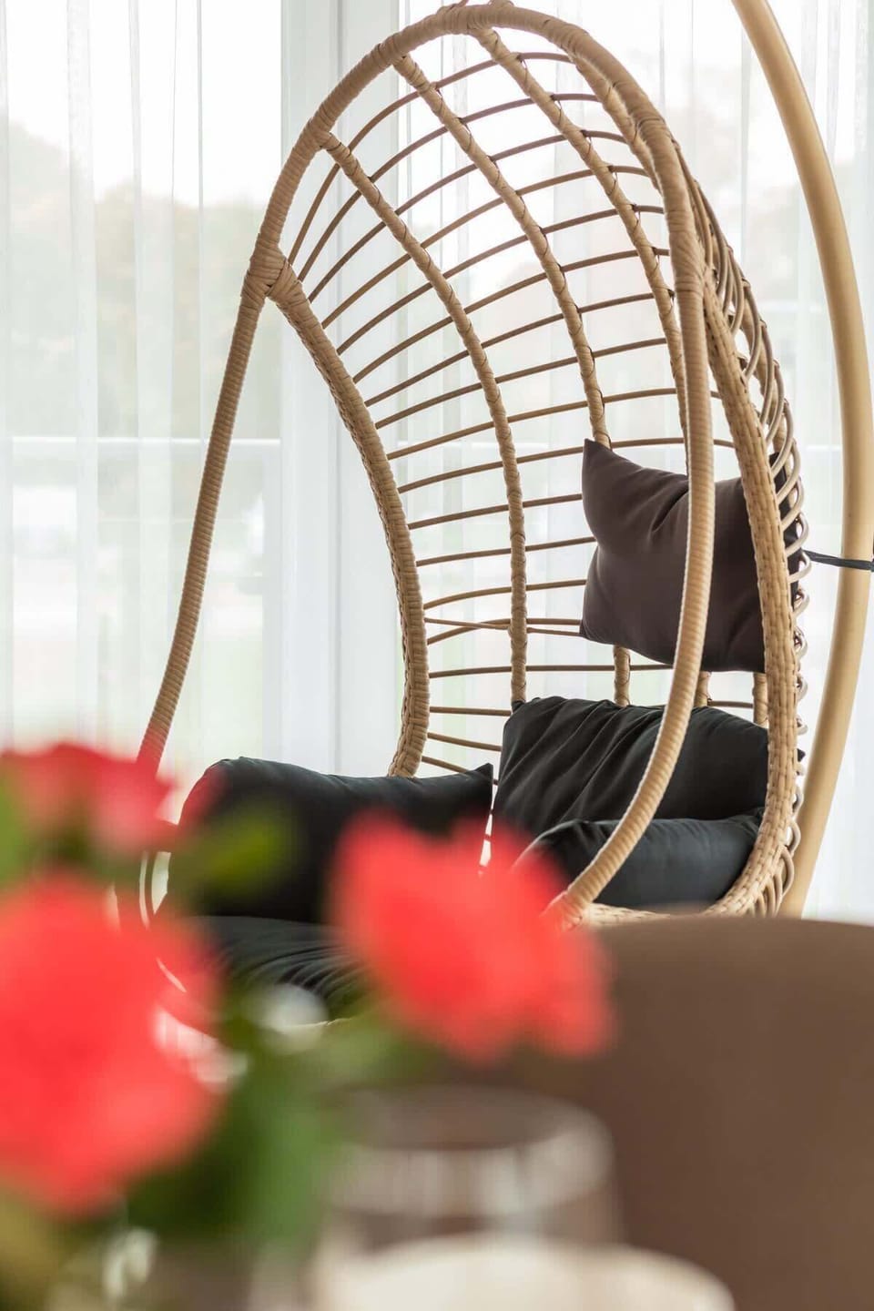 A decorative corner featuring a stylish hanging chair and red roses in the foreground.
