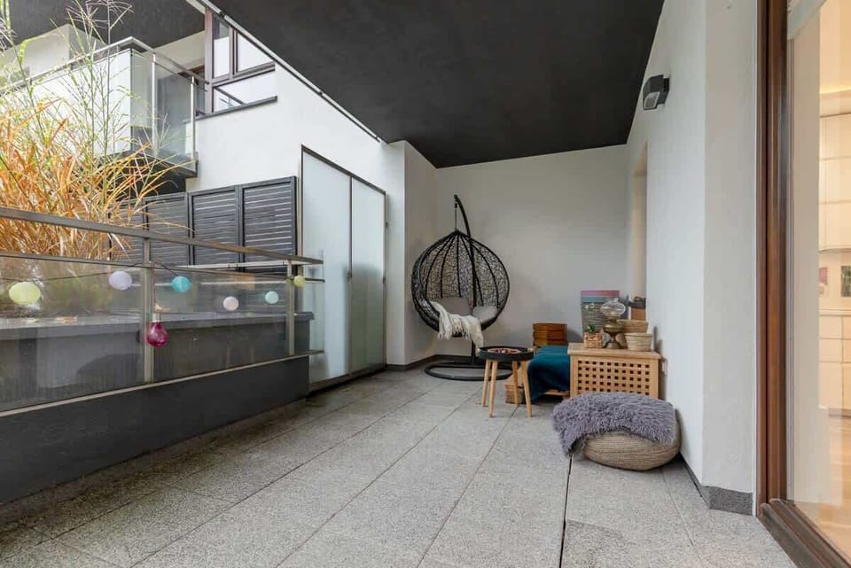 A spacious balcony with outdoor seating, a hanging chair, and decorative plants.
