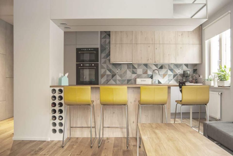 A stylish kitchen with a breakfast bar, wooden cabinets, and yellow bar stools.
