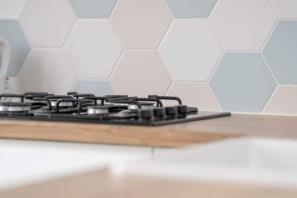 A detailed shot of the kitchen gas stove, featuring a hexagonal tile backsplash in soft pastel tones.
