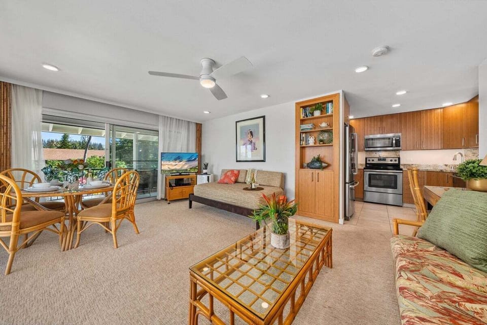 Open living space with ocean views — rattan furniture, ceiling fan, and framed art create a breezy island vibe.