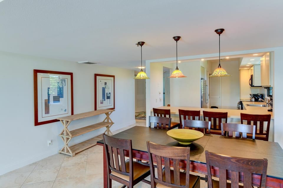 Pendant lights hang above a kitchen pass-through with a breakfast bar and four wooden chairs.