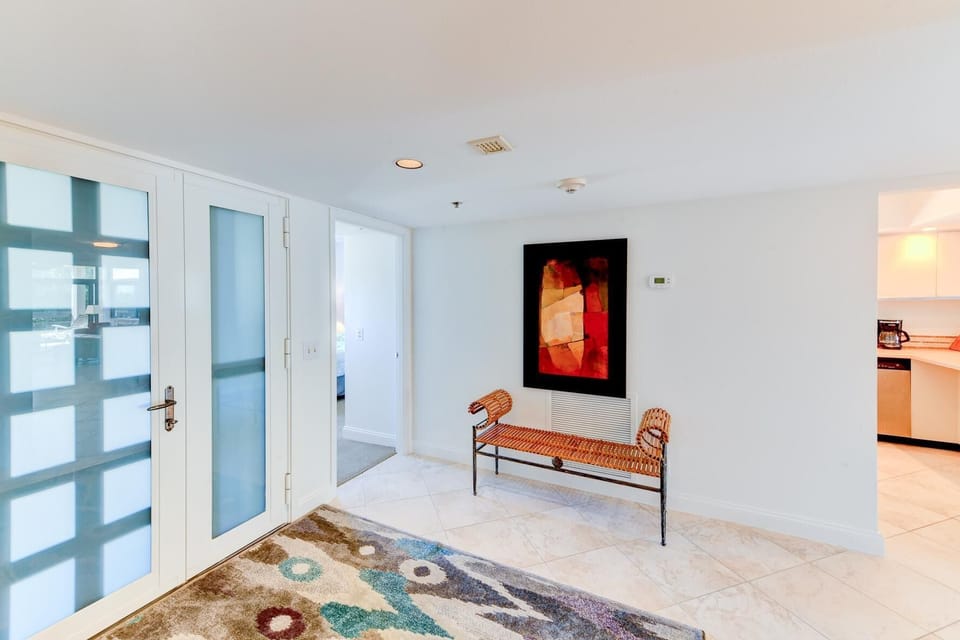 Entryway with frosted glass double doors, a patterned area rug, and a woven bench beneath abstract artwork.