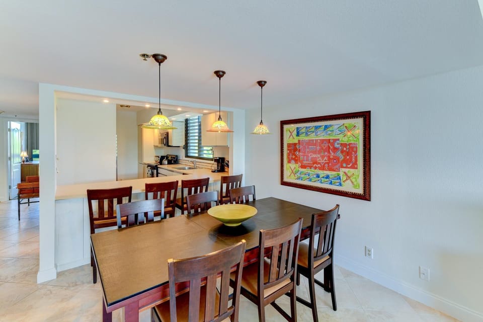 Dark wood dining table seats eight beneath colorful pendant lights and a large framed artwork.
