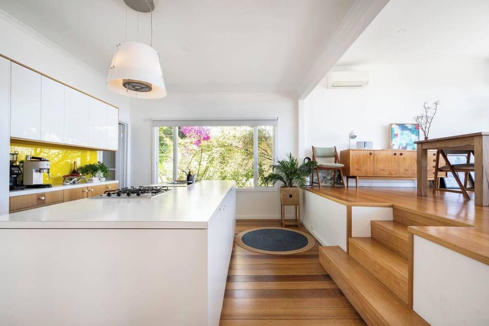 A mezzanine level features a light-filled dining area, with floor-to-ceiling windows capturing views overlooking the balcony and out to the bay. 
