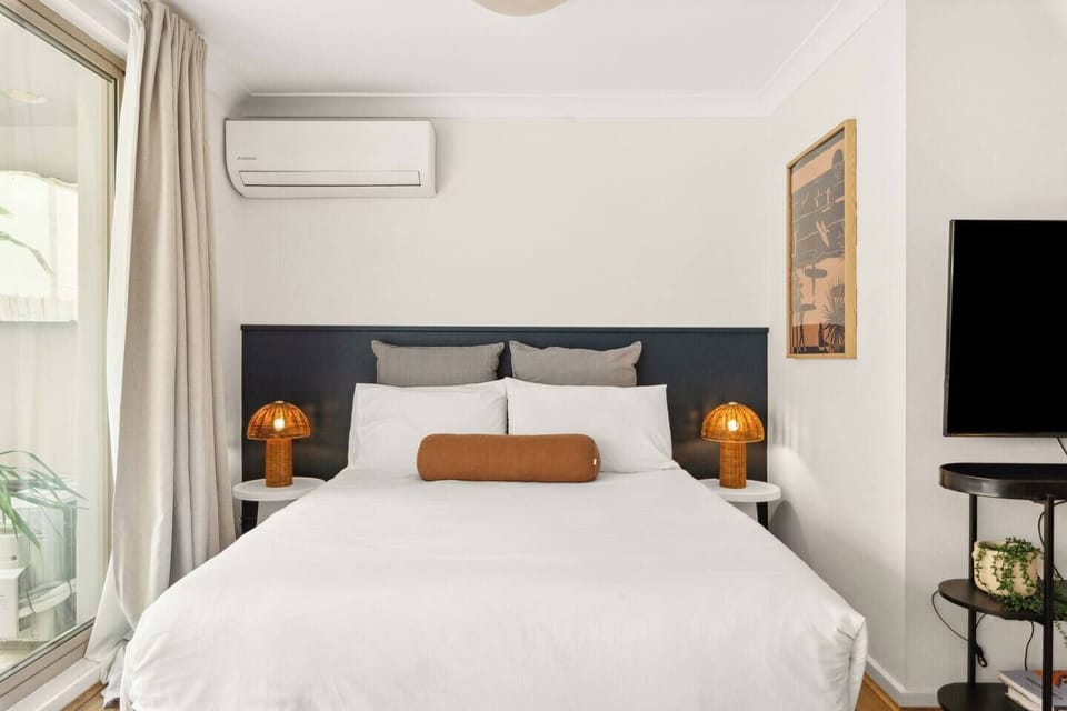 Relax in the queen-sized bed with a balcony view. You'll find two bedside lamps for added convenience and a stylish frame nearby, along with an air conditioning split system for year-round comfort.