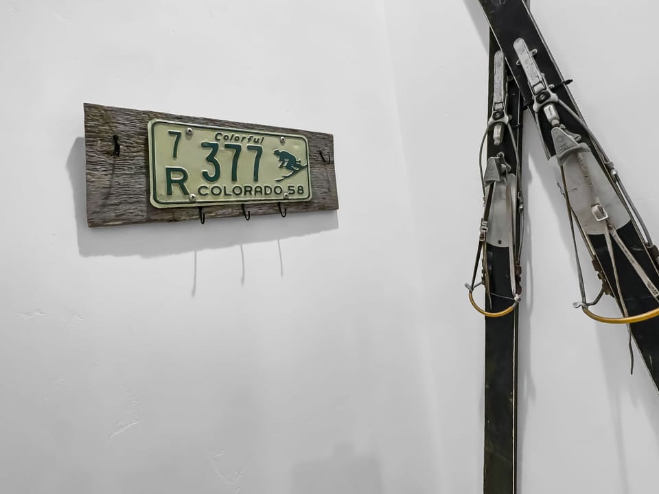An old Colorado license plate from 1958 mounted on wood and a pair of vintage skis hung on a white wall.