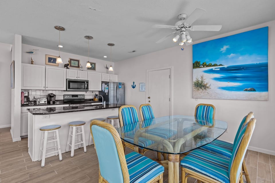 Your open-concept kitchen flows into a bright dining area, where tropical-themed seating and ocean artwork create a breezy coastal vibe for memorable meals.