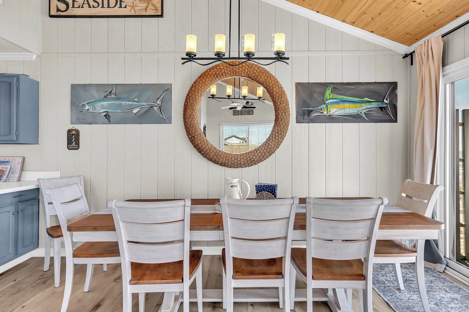 Gather around this inviting table in your coastal-themed dining space. Nautical artwork, a woven mirror, and warm lighting create a relaxed atmosphere perfect for sharing meals and making memories with loved ones.