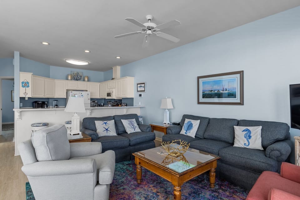 Relax in your coastal-themed living space with soft blue walls, comfortable seating, and a fully equipped kitchen for preparing meals together.