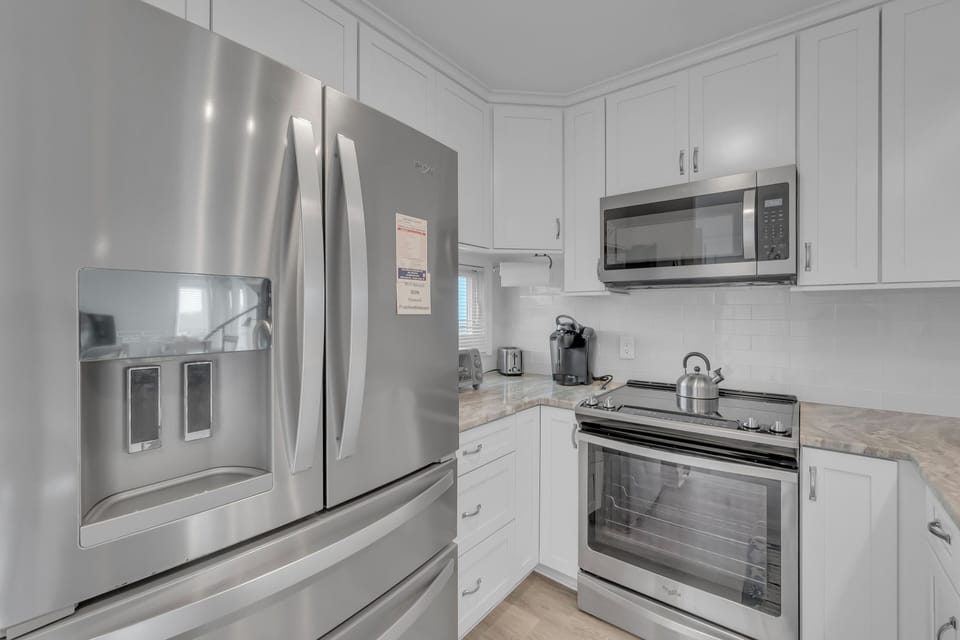 Your fully equipped kitchen features modern stainless steel appliances and pristine white cabinets, perfect for preparing memorable meals during your stay.