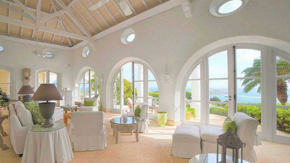 Large, high-ceilinged space well-appointed with comfortable off­-white sofas and armchairs with sage-green cushions. Wide, arched French doors open on three sides to let in sunlight and the ocean breeze. Opens onto the terrace, pool and ocean view on one 