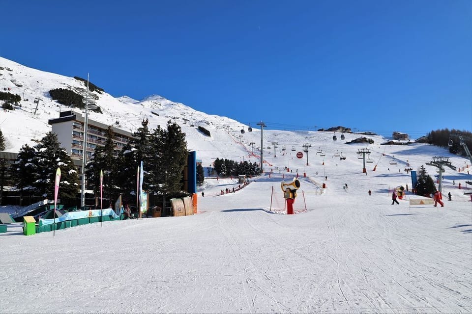 The lively ski-in area at the residence, with colourful banners and the slopes of Les Menuires right outside.