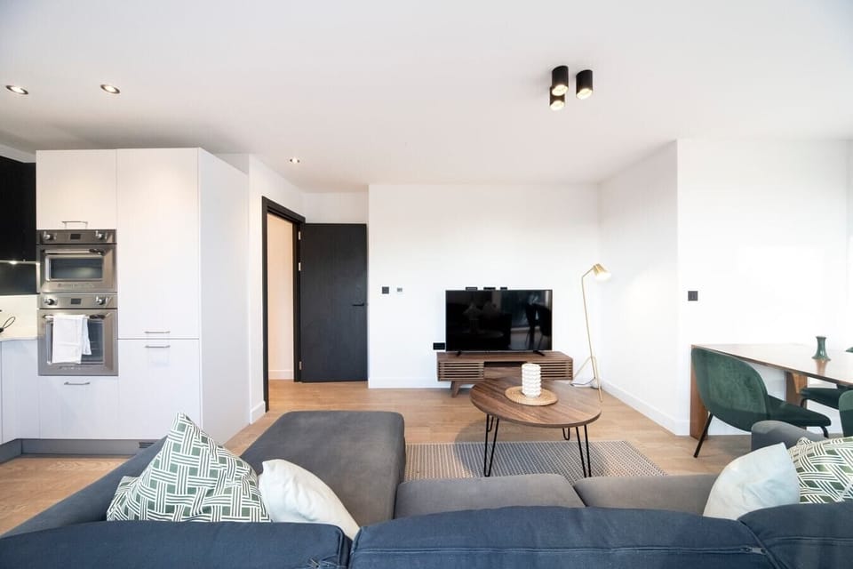 The bright living room features a pull-out sofa bed, a Smart TV, a dining table and chairs, and a small balcony