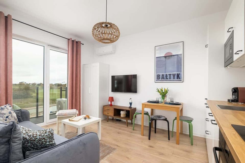 A living area with a mounted TV, wooden cabinets, and a small dining setup in the background.

