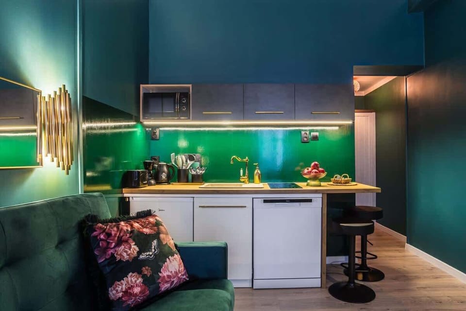 A compact living space with a kitchenette, a dark green sofa, and under-cabinet lighting.


