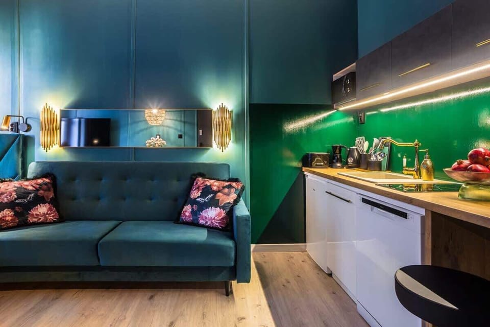 A compact living space with a kitchenette, a dark green sofa, and under-cabinet lighting.

