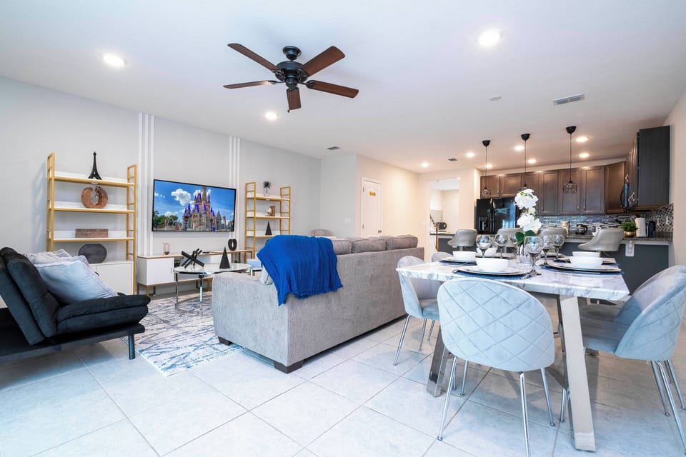 Experience a bright and inviting living space with a cozy sectional sofa and a vibrant blue throw. The open layout connects the chic dining area and sleek kitchen, offering a perfect flow for relaxation and dining.