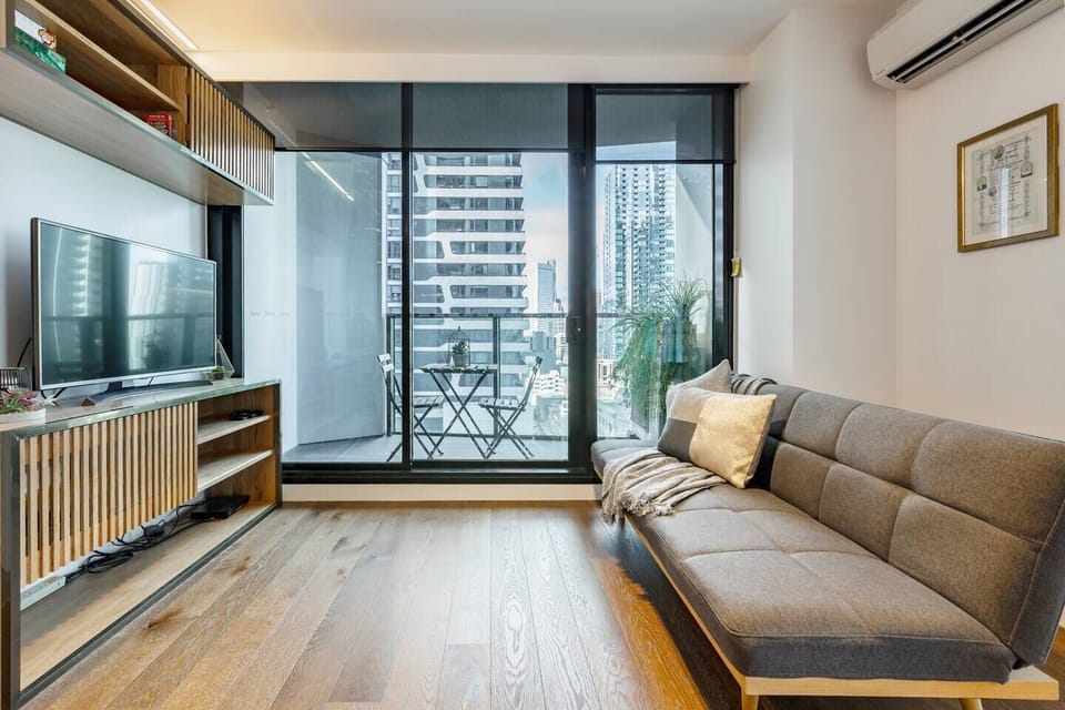 A comfortable lounge room sits alongside floor-to-ceiling windows and glass doors with views looking out through the city